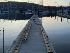 Close-up of marina construction showing new piles being installed into rocky seabed, with assembled pontoons floating nearby.