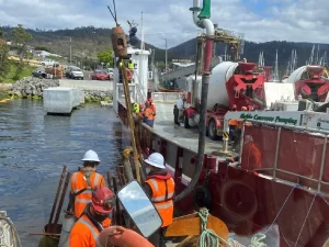 Construction of ferry dolphins with heavy-duty piles and platforms in place, set against a backdrop of calm waters and distant shoreline.