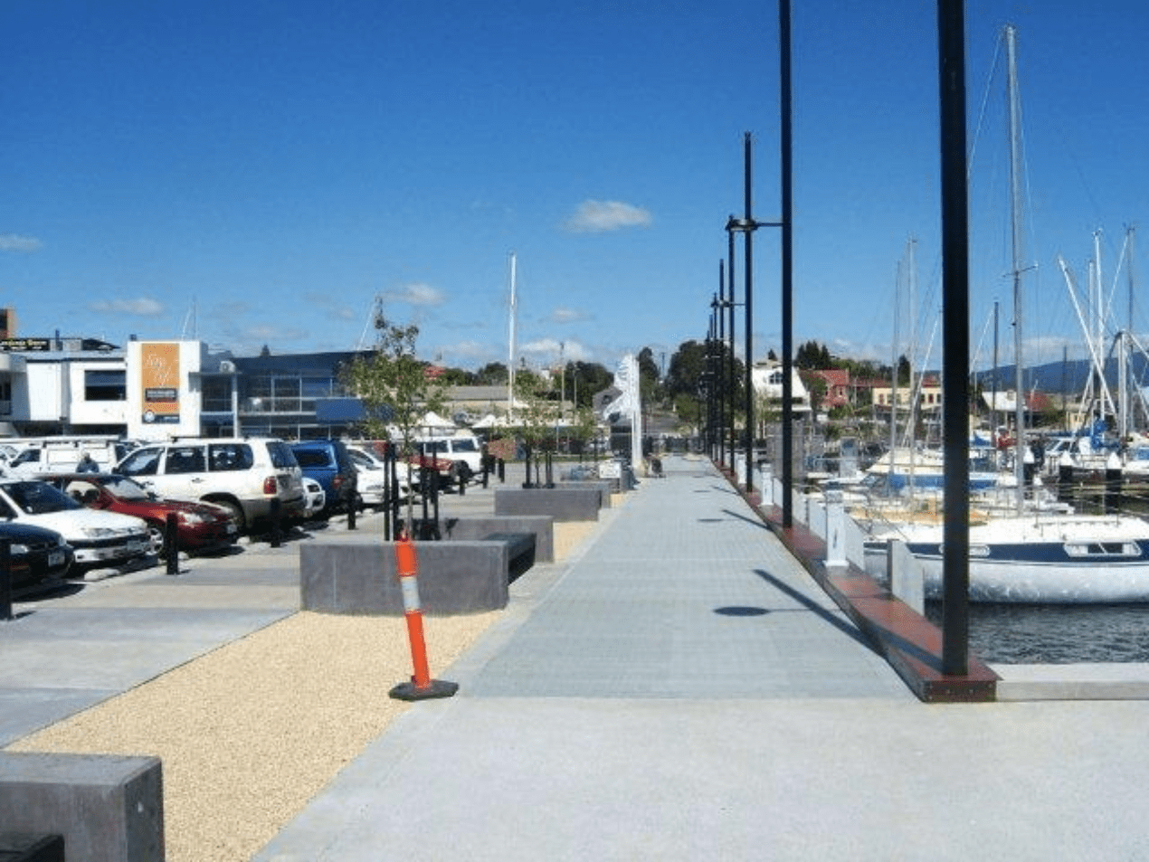 A view of a marina with several boats and cars lined up on the sidewalk.