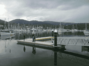 Two people are standing on a dock, enjoying the view of the water and surrounding scenery.