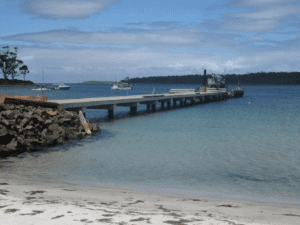 A scenic pier with boats docked on the water, alongside a sandy beach under a clear blue sky.